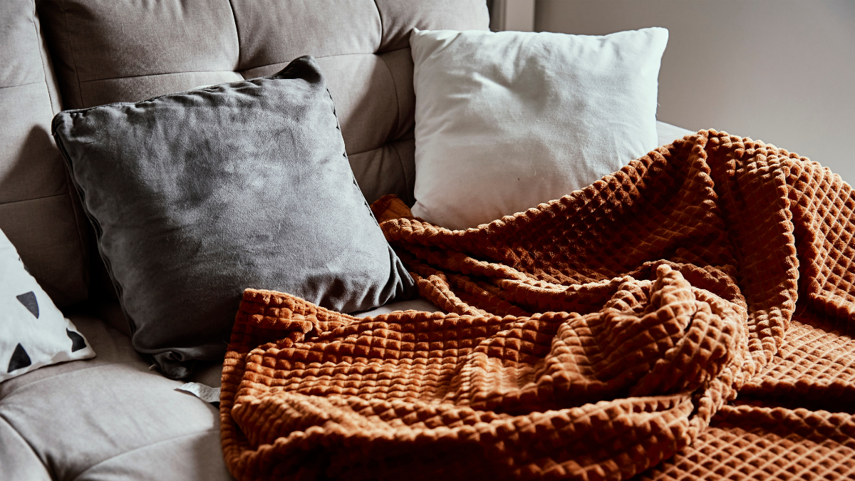 A cozy seating area with soft grey and white pillows paired with a warm, textured orange blanket. The perfect setup for a relaxed and inviting atmosphere.