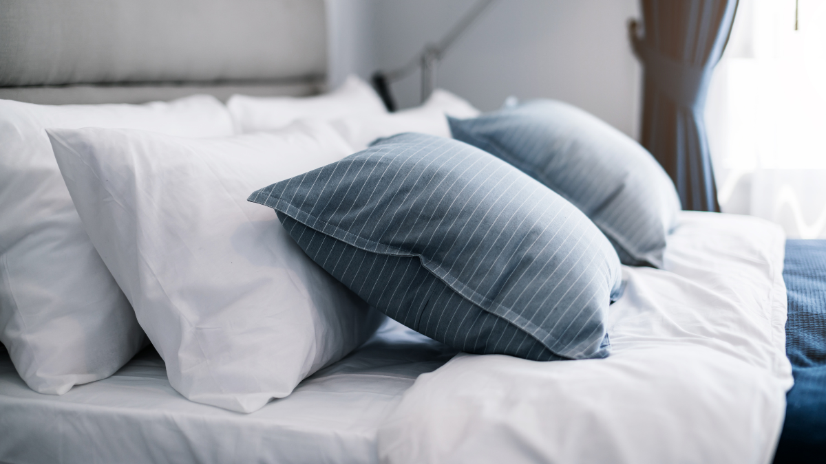 A modern bedroom setup with a neatly arranged bed featuring crisp white sheets and pillows, complemented by blue, striped pillowcases.