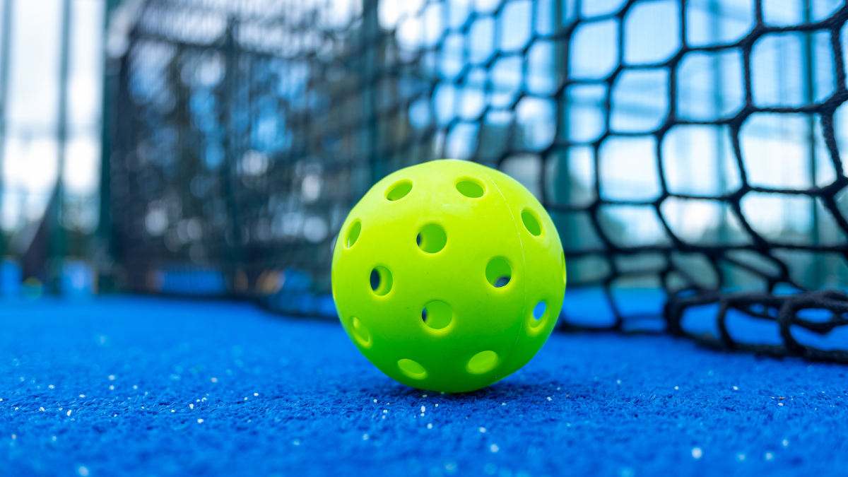 This close-up image showcases a bright green pickleball resting on a blue court surface, with a blurred net in the background, highlighting the focus on the game.