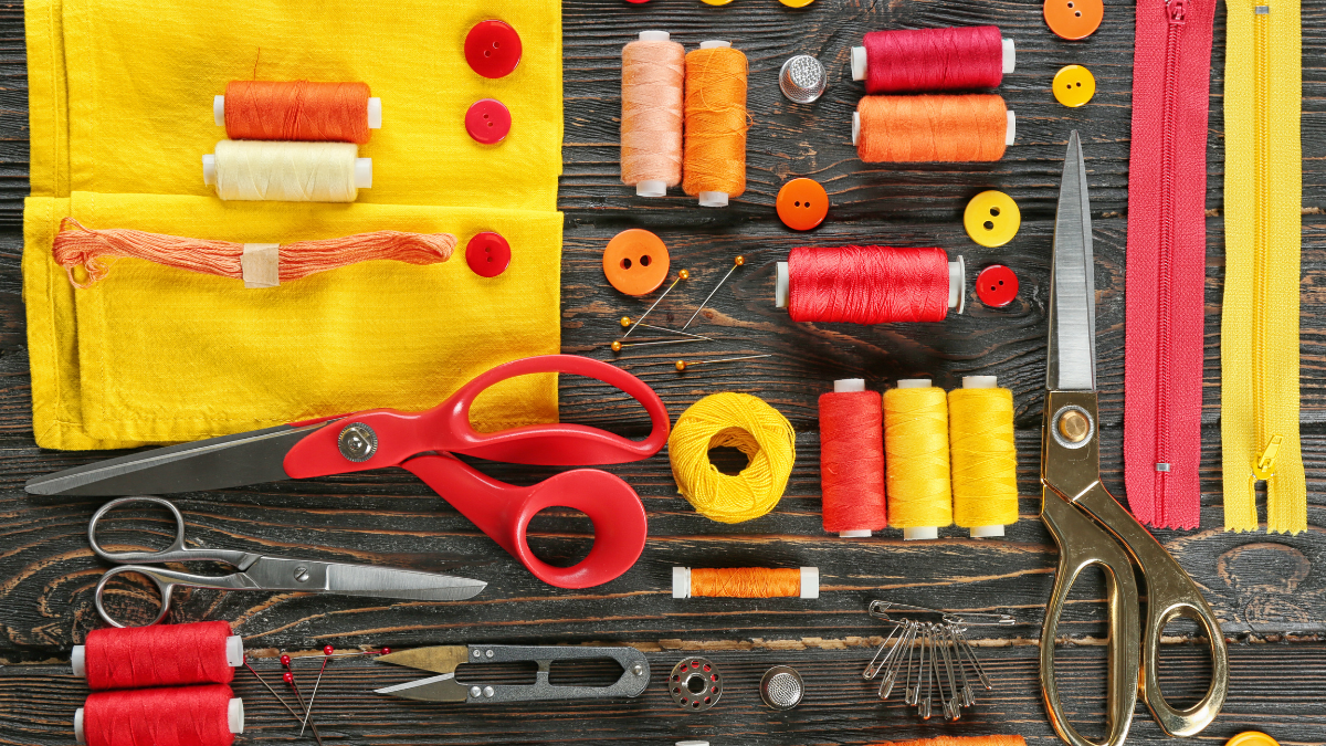 Vibrant sewing supplies flat lay featuring colorful spools of thread, fabric swatches, scissors, buttons, zippers, and sewing pins arranged on a rustic wooden background.