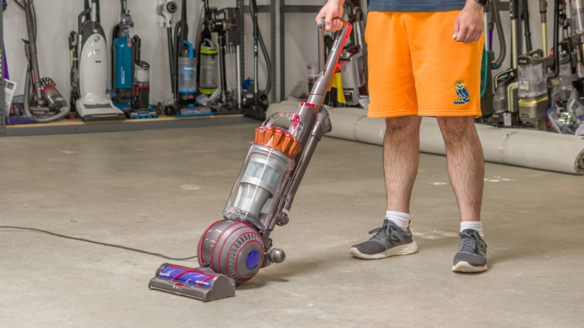 Person in orange shorts operating a modern upright vacuum cleaner in a store filled with cleaning equipment.