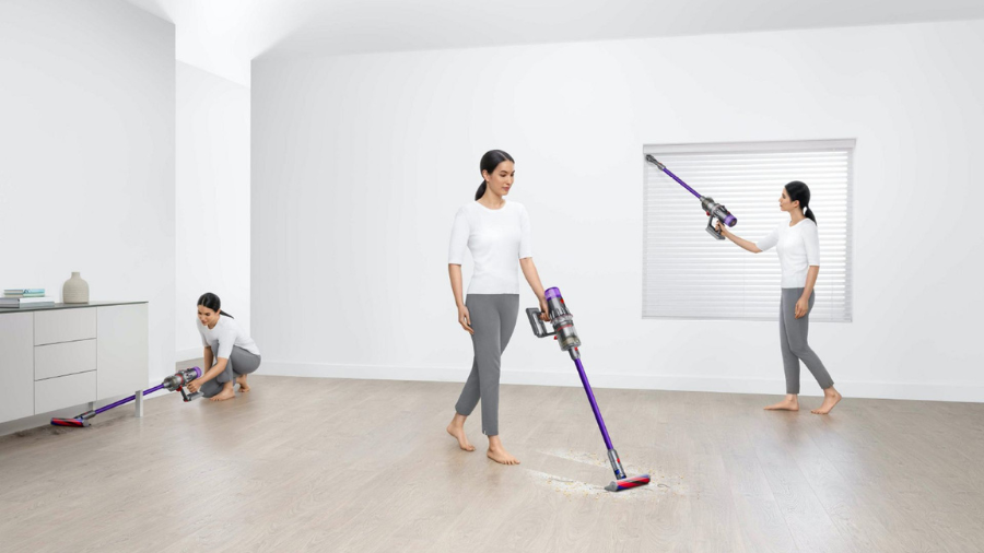 A woman using a cordless vacuum cleaner in various modes to clean a minimalistic white room with a hardwood floor.