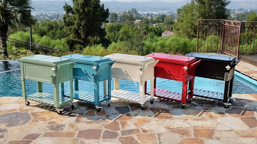 A lineup of colorful rolling patio coolers, including teal, light blue, white, red, and black, placed by a poolside with a scenic outdoor view.
