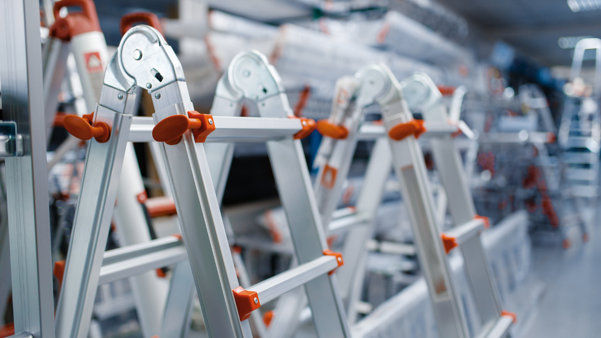 A row of foldable aluminum ladders with orange accents displayed in a hardware store.