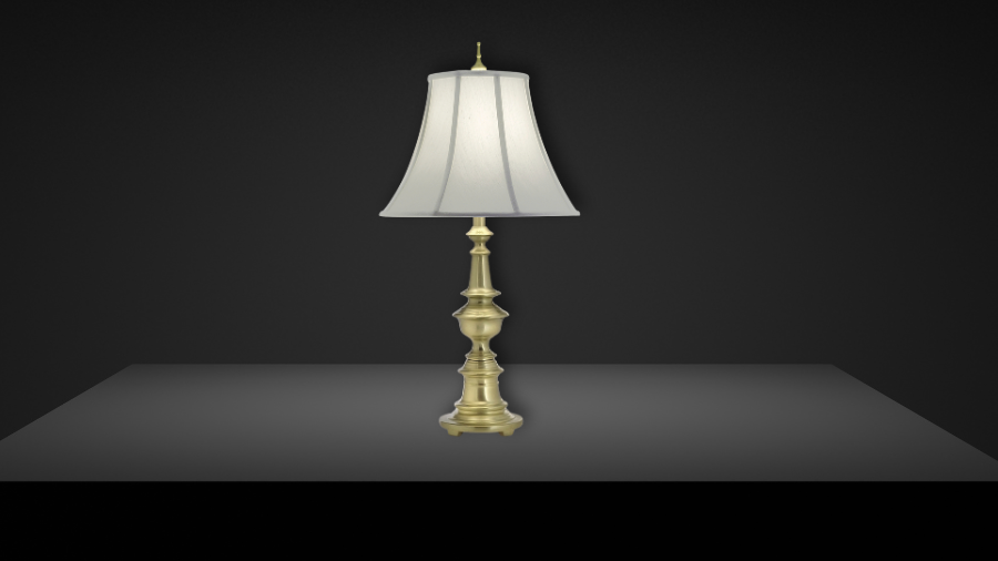 A classic table lamp with an ornate brass base and a white bell-shaped fabric shade, set against a dark background on a smooth surface.