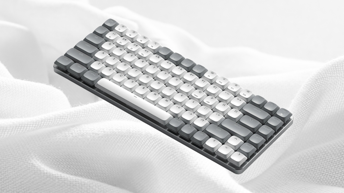 A compact gray and white mechanical keyboard is placed on a soft white fabric background.