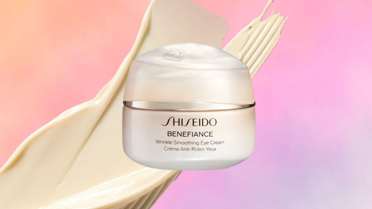 A jar of Shiseido Benefiance Wrinkle Smoothing Eye Cream is displayed against a soft pink and peach gradient background, with a creamy texture swatched behind it.
