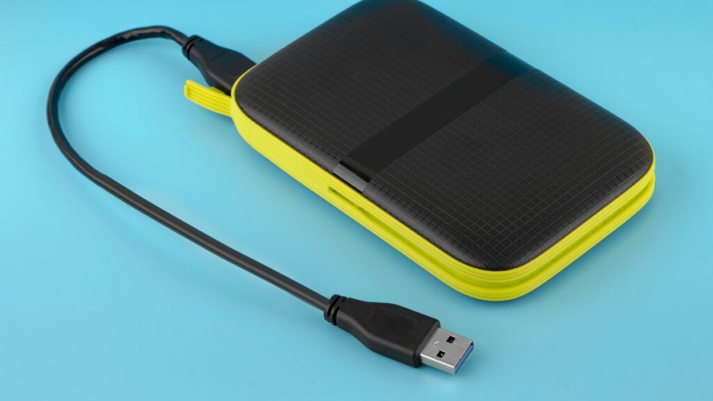 Black and yellow external hard drive with USB cable, placed on a light blue background.