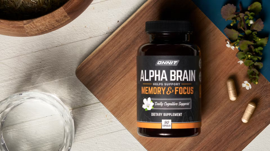 Bottle of Alpha Brain dietary supplement on a wooden board, surrounded by capsules, a glass of water, and herbs.