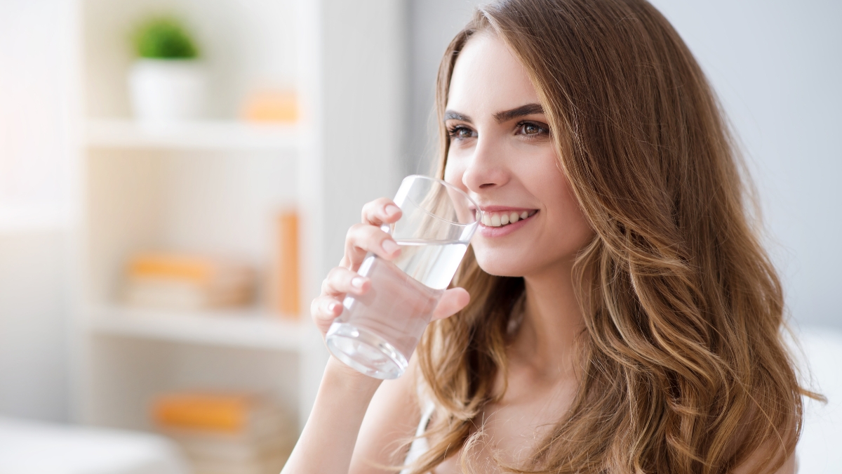 Woman smiling while drinking a glass of clean water at home.