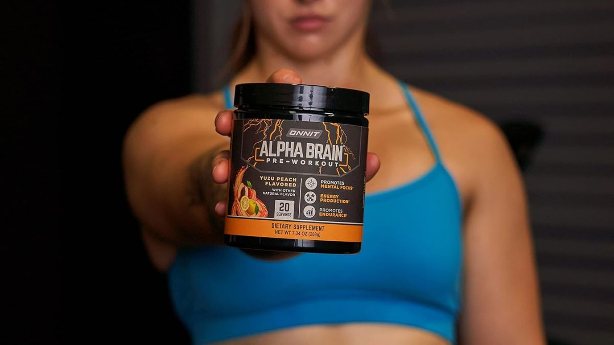 Woman holding out a container of Alpha Brain pre-workout supplement in yuzu peach flavor.