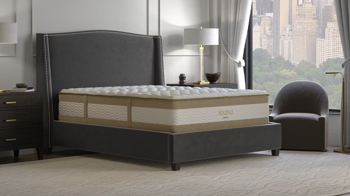 A Saatva mattress on a dark bed frame in an upscale city-view bedroom.