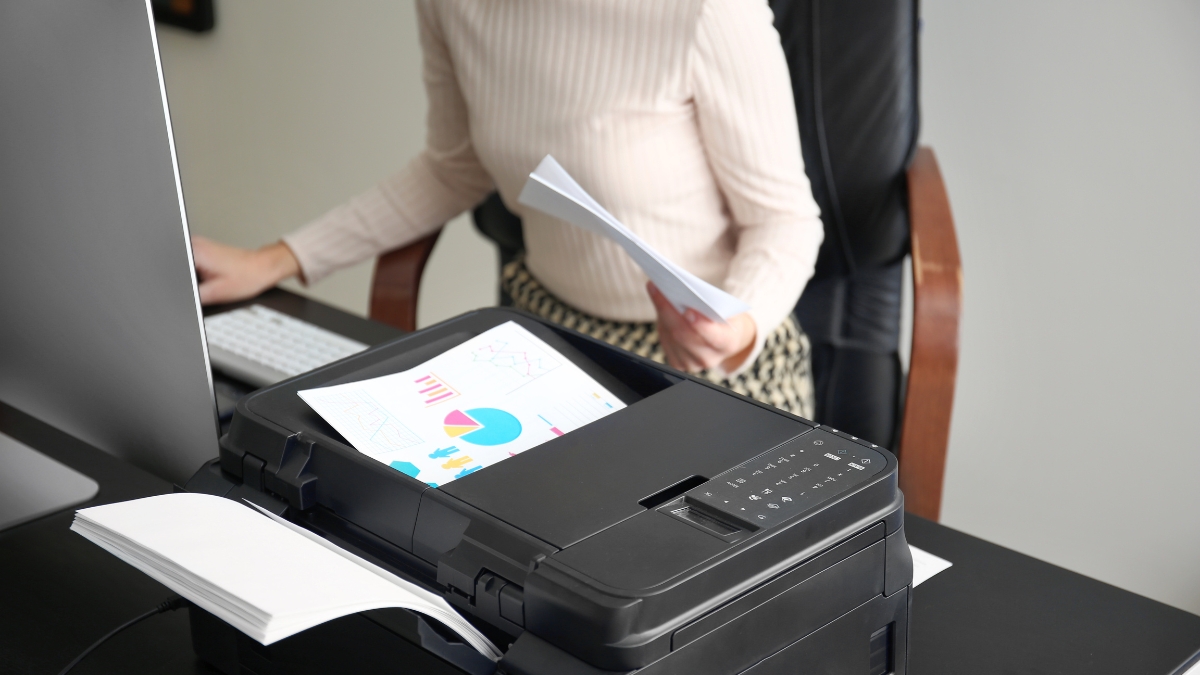 A woman uses a home office setup with a color chart printing from an HP OfficeJet Pro 6978 printer.