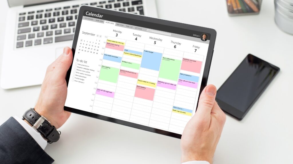 Person holding a tablet with a digital calendar display showing a full weekly schedule and to-do list.