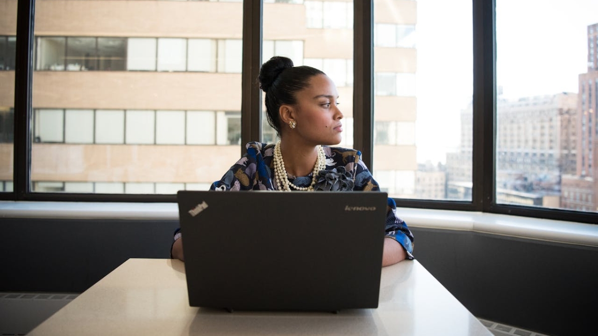 Woman working on a Lenovo ThinkPad laptop at a bright office table with city buildings in the background.
