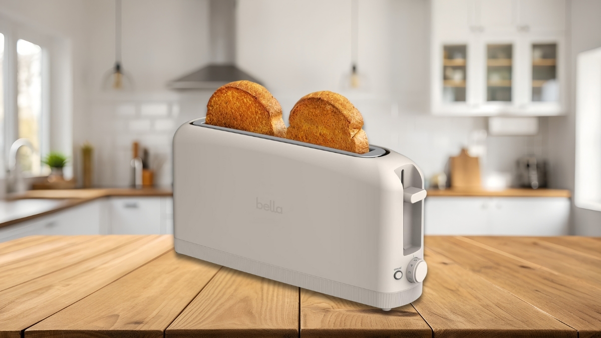 Bella 2 Slice Slim Toaster on a wooden kitchen counter with two slices of golden-brown toast, showing its ultra-slim design and long slot in a bright modern kitchen.